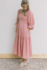 Model wearing a rose dress with pink flowers, pockets, poet sleeves and a smocked bodice.