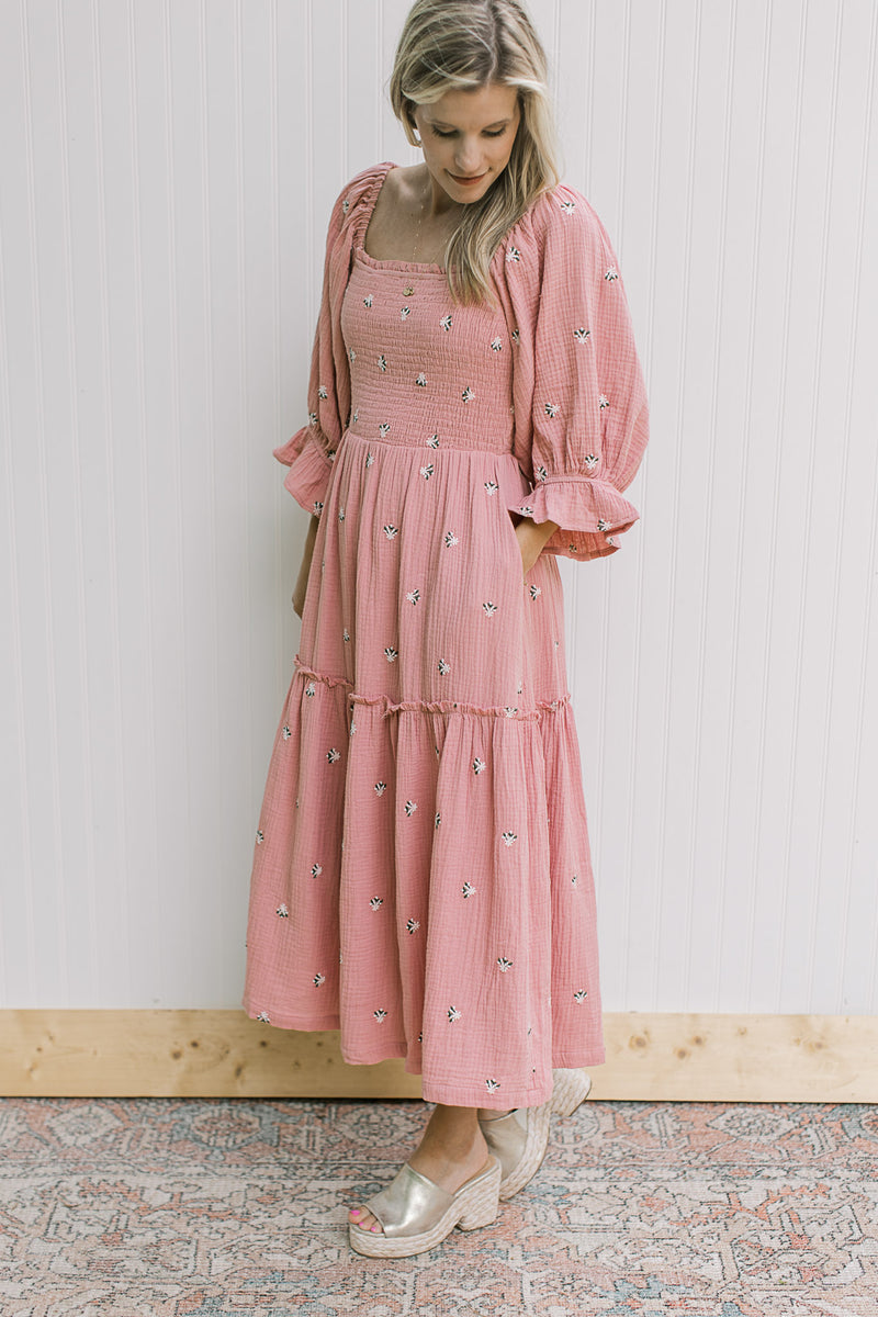 Model wearing a rose dress with pink flowers, pockets, poet sleeves and a smocked bodice.