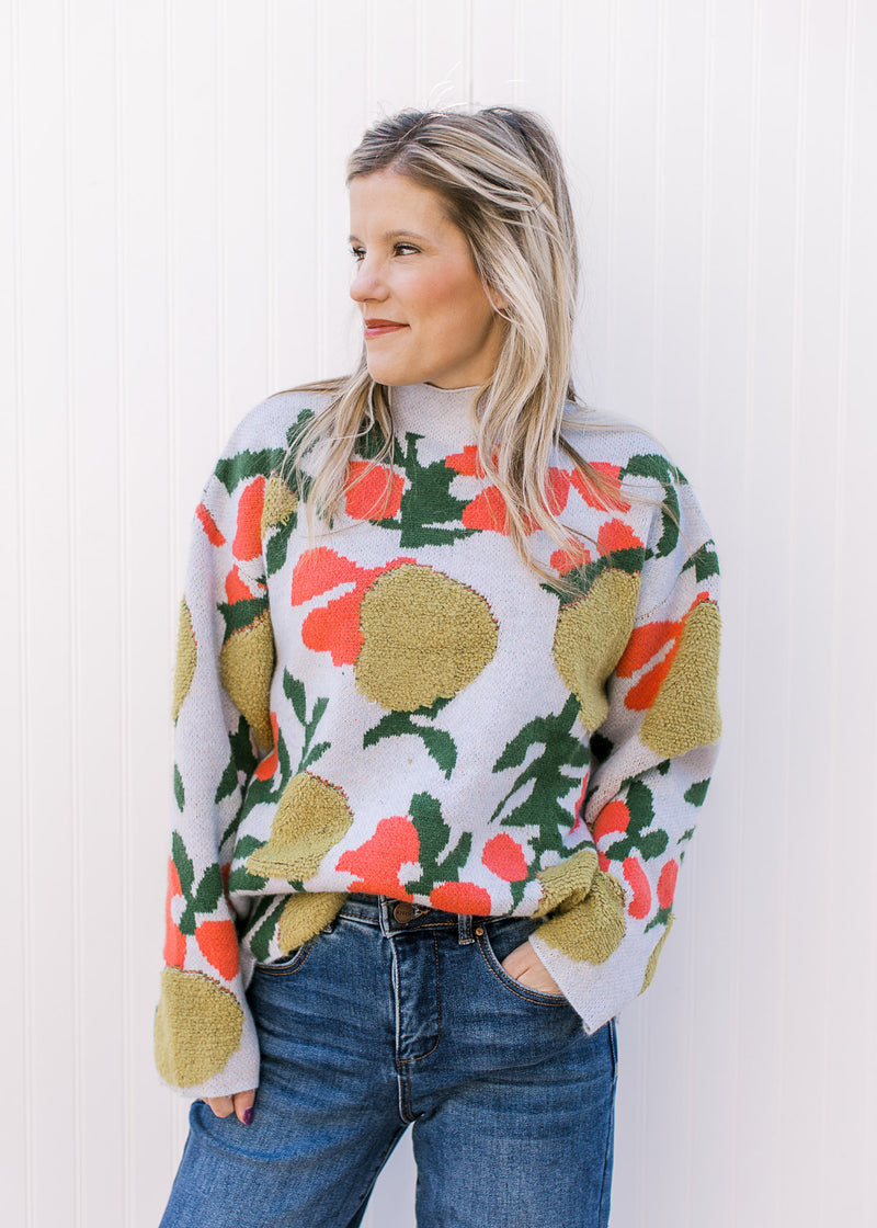 Model wearing a oversized baby blue sweater with bright floral a mock neck and long sleeves.