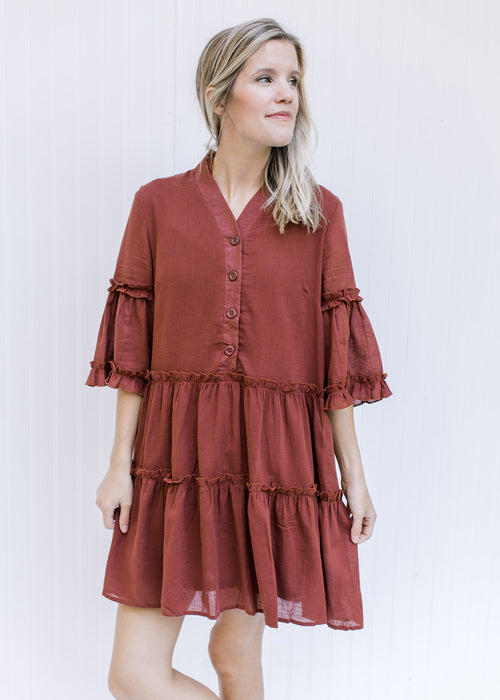 Model wearing a brick colored above the knee dress with pockets and 3/4 butterfly sleeves. 