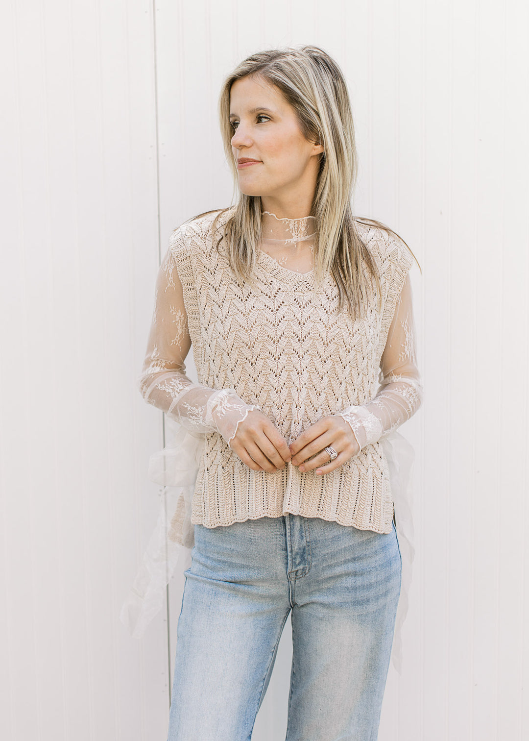 Model wearing an oatmeal sleeveless v-neck with ribbon side tie closures and a knit material. 