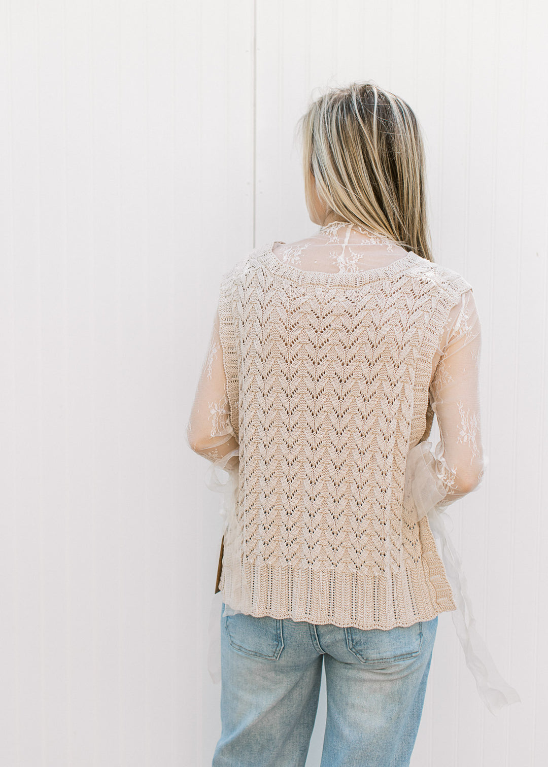 Back view of Model wearing an oatmeal sleeveless knit with ribbon side tie closures. 