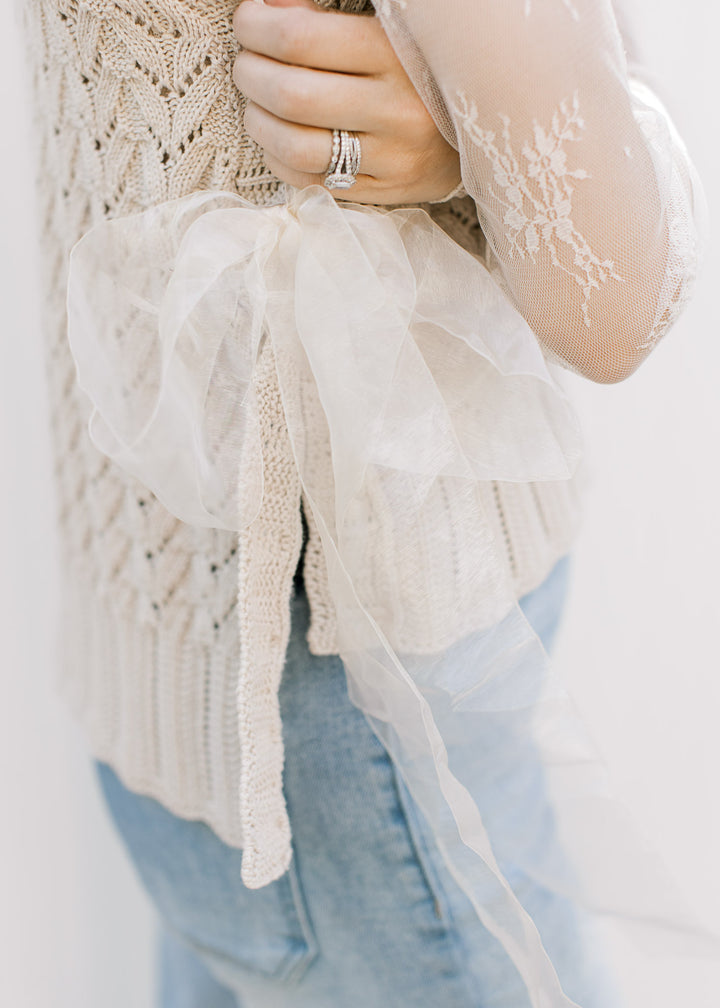 Close up of ribbon side tie closure on a sleeveless knit v-neck with high low fit. 