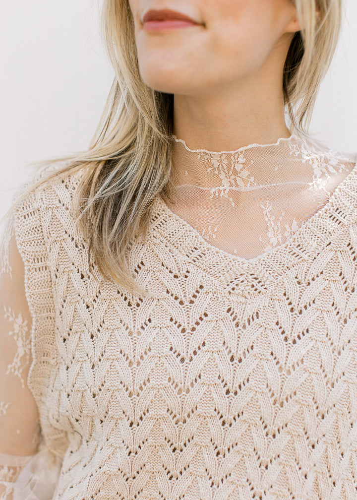 Close up of v-neck and open knit on a sleeveless oatmeal colored top with side tie closure. 