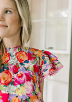 Close up view of flutter short sleeves with lace and ruffle neck on a bright floral top.