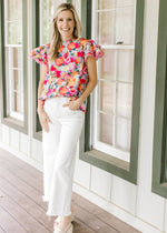 Model wearing a cotton bright floral top with flutter short sleeves with lace and ruffle neck.