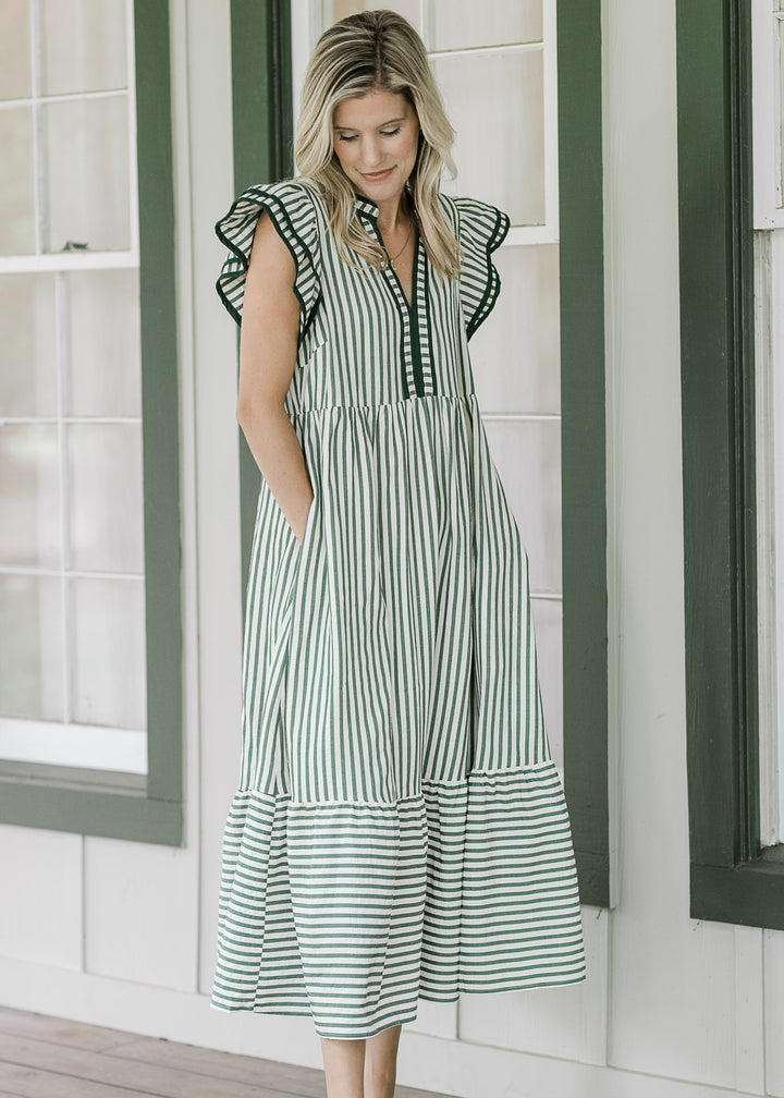 Model wearing a cream v-neck dress with green stripes, pockets and layered flutter cap sleeves. 