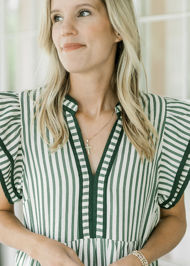 Close up of v-neck and layered flutter cap sleeves on a cream mid with green stripes. 