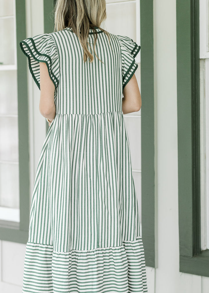 Back view of Model wearing a cream dress with pink colored stripes and layered flutter cap sleeves. 