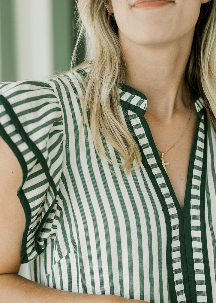 Close up of pine piping along flutter cap sleeves and v-neck of a cream midi with green stripes.