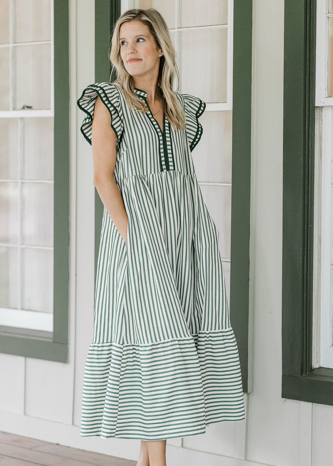 Model wearing a cream v-neck dress with pink colored stripes and layered flutter cap sleeves. 