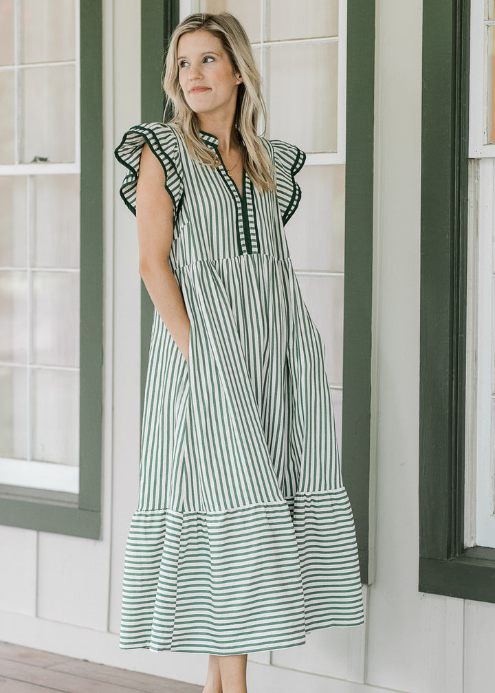 Model wearing a cream v-neck dress with pink colored stripes and layered flutter cap sleeves. 