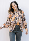 Model wearing a cream button up with brown and orange flowers, long sleeves and a collar. 