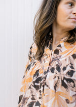 Close up of buttons and pleating along yolk on a cream top with orange and brown flowers. 