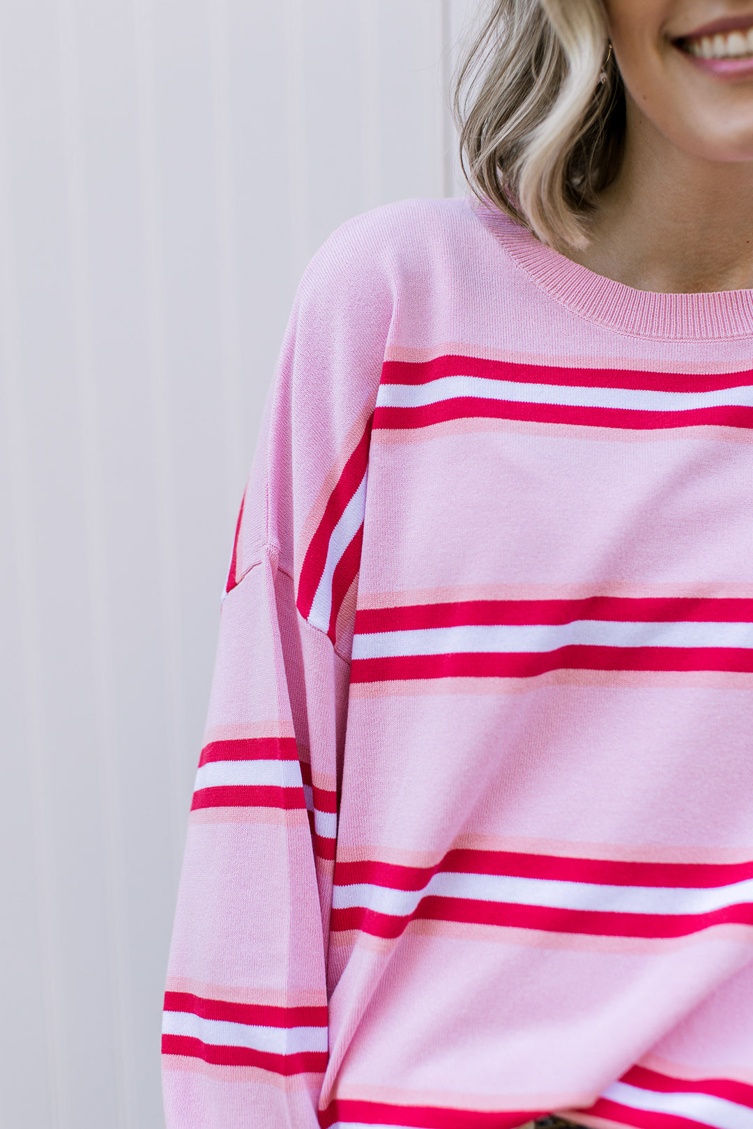 Close up of red and white stripes on a pink sweater with long sleeves and a round neckline. 