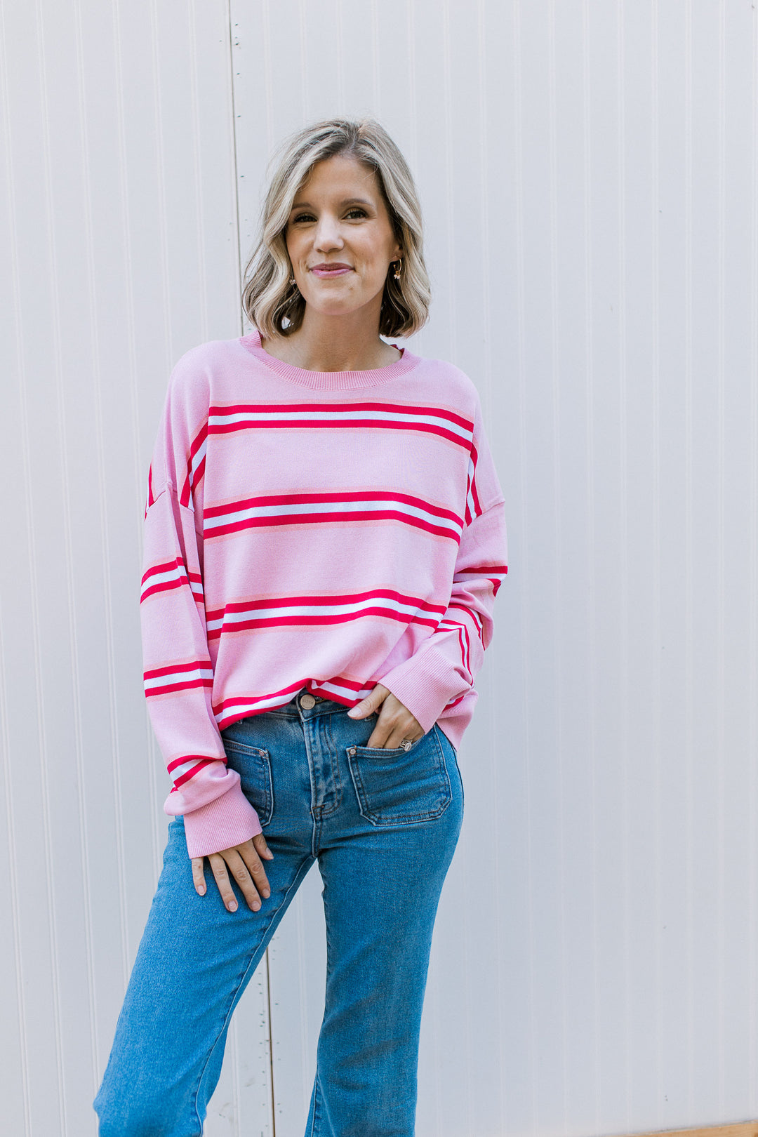 Model wearing a pink sweater with red and white stripes, round neck and long sleeves.