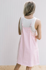 Back view of Model wearing a fully lined pink romper with adjustable straps and front patch pockets.