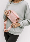 Model holding a pink crossbody belt bag with two pockets and gold clasp. 