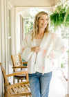 Model wearing a cream yarn cardigan with crochet pink bows and an open front. 