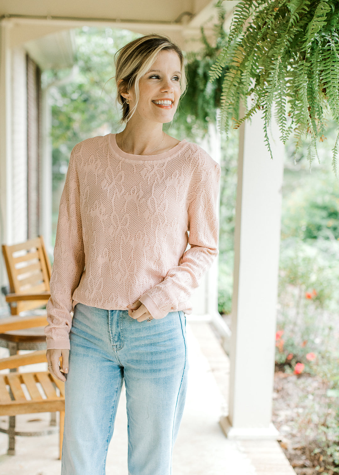 Model wearing a blush sweater with loose knit, floral design and long sleeves. 