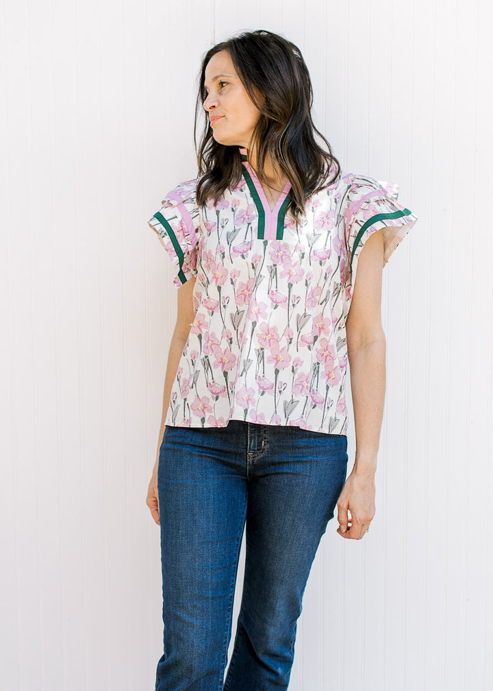 Model wearing jeans and a cream top with pink and green floral, v-neck and short ruffle sleeves. 