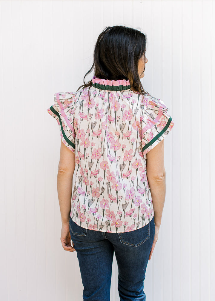 Back view of Model wearing a cream top with pink and green floral and ruffle neck and sleeves. 