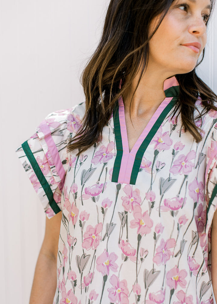 Close up of pink and hunter trim at neck and short sleeves of a cream top with floral. 
