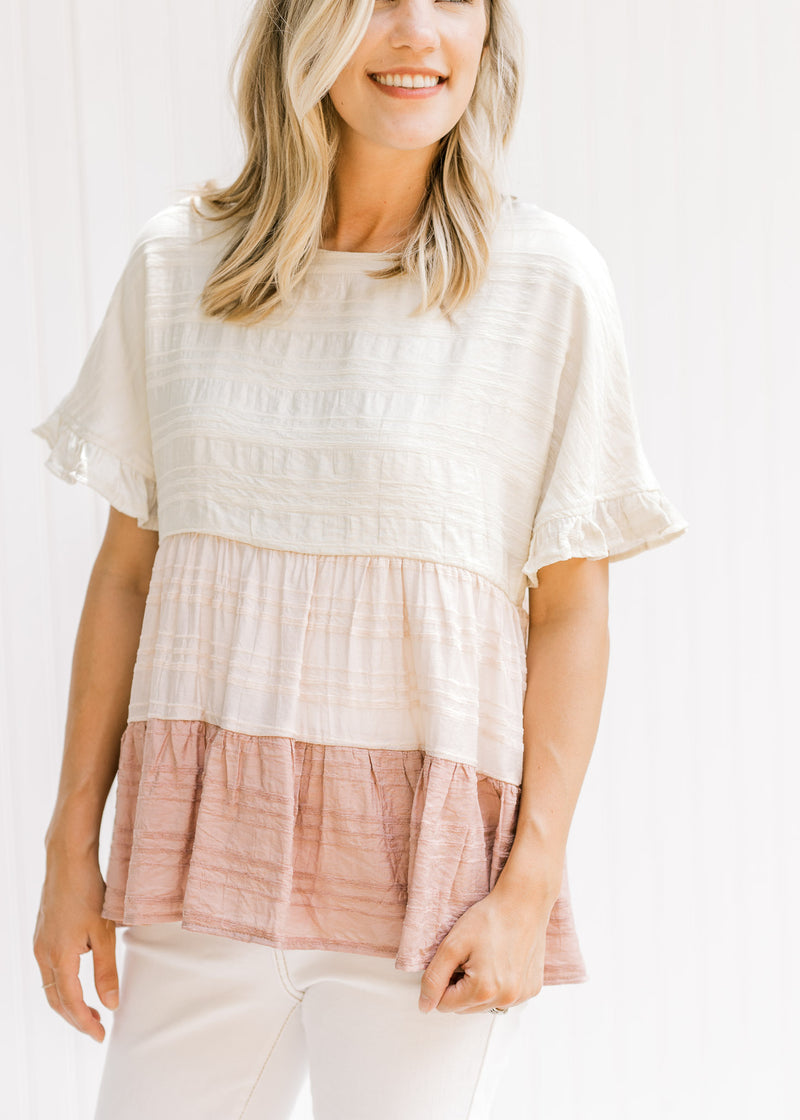 Model wearing a cream, light pink and mauve tiered colorblock top with short sleeves.
