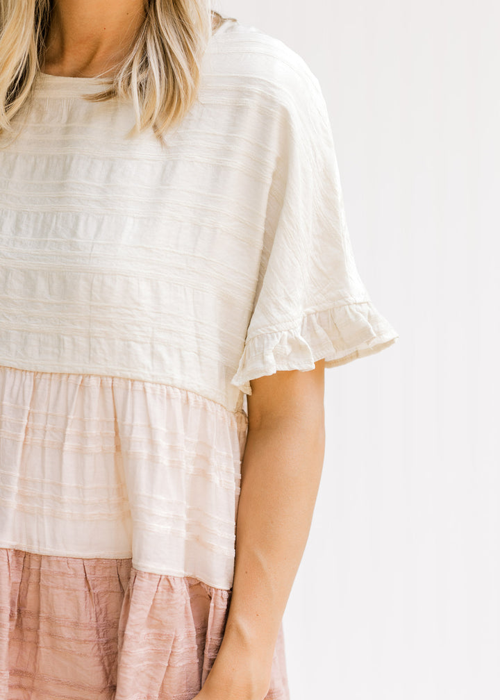Close up view of ruffle on short sleeve of a cream, light pink and mauve colorblock top.
