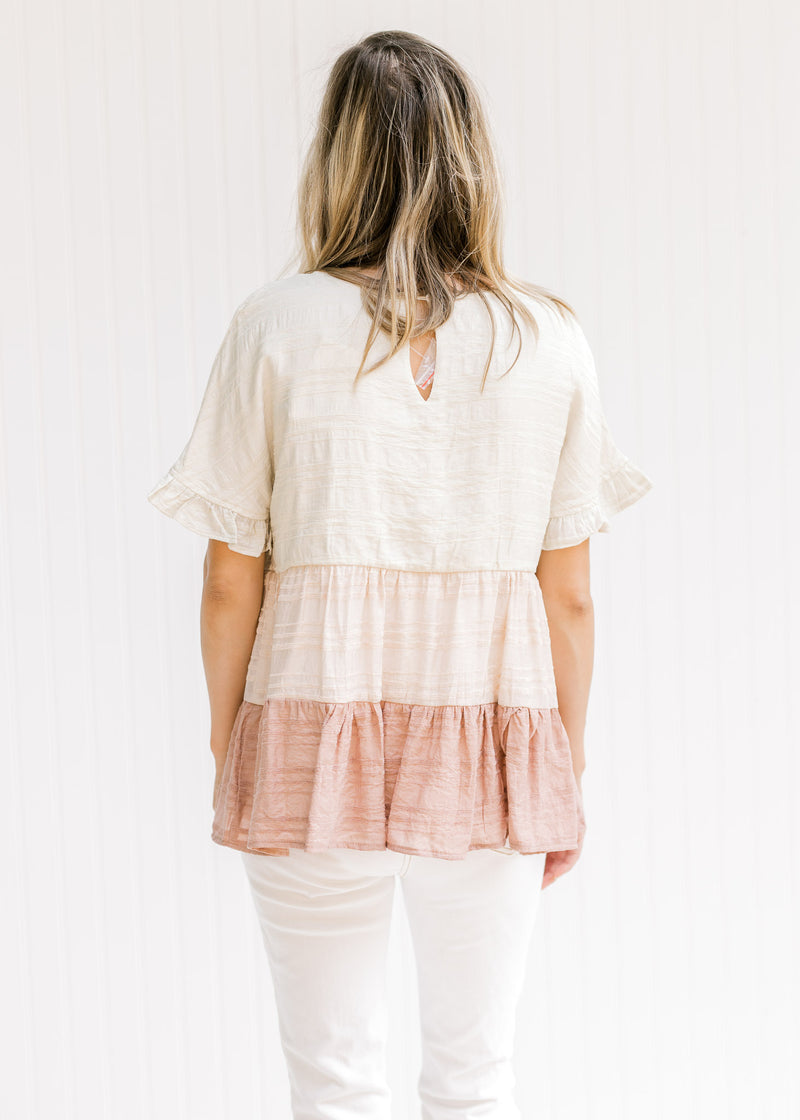 Back view of Model wearing a cream, light pink and mauve tiered colorblock top with short sleeves.