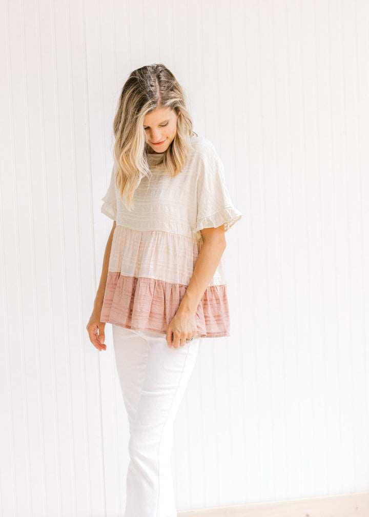 Model wearing white jeans with a cream, light pink and mauve colorblock top with short sleeves.