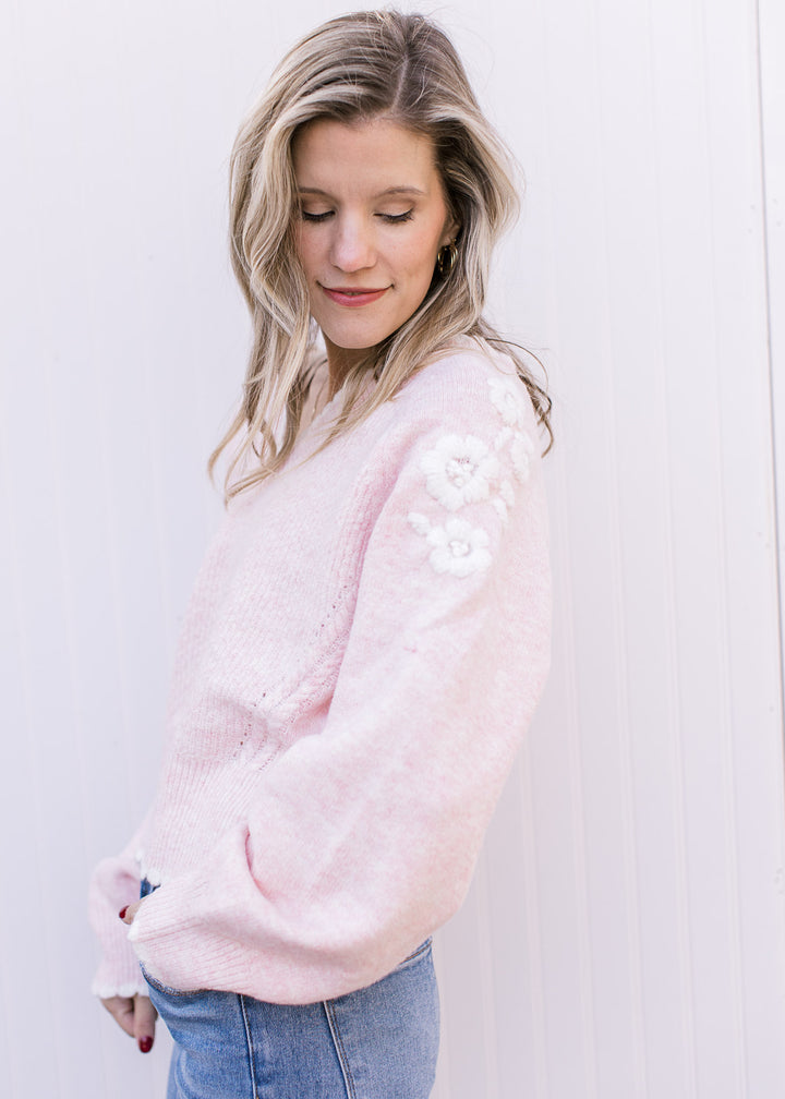 Model wearing a soft pink sweater with scalloped v-neck and yarn floral embroidery at shoulder.