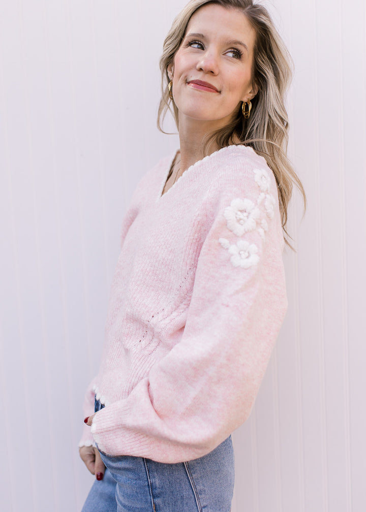 Side view of Model wearing a pink sweater with scalloped v-neck and yarn embroidery at shoulder