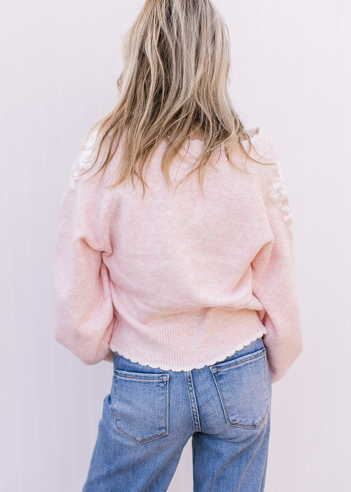 Back view of Model wearing a soft pink sweater with scalloped hem and yarn embroidery at shoulder.