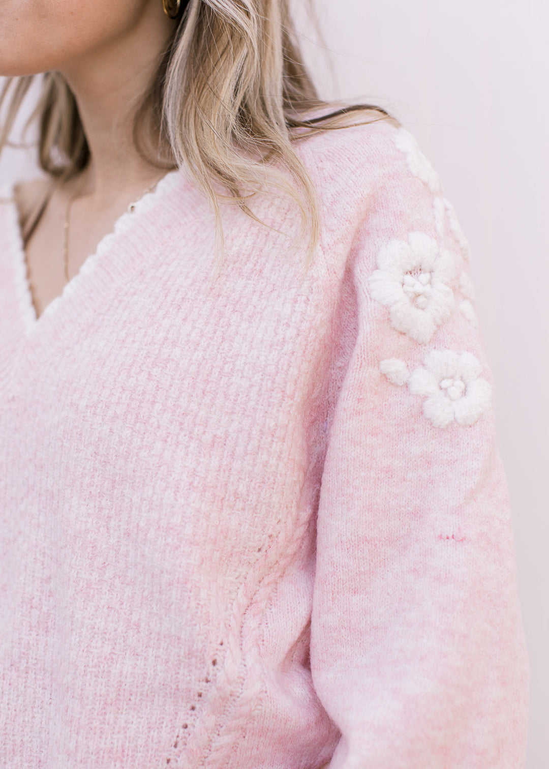 Close up of cream yarn floral embroidery at the shoulder on a soft pink long sleeve sweater. 
