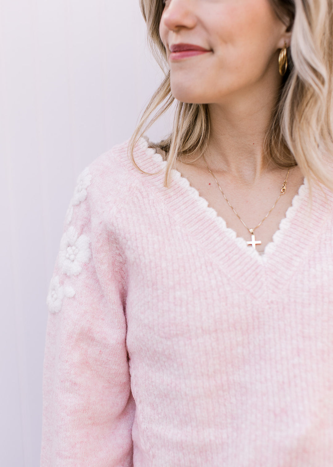 Close up of v-neck with white scalloped trim on a soft pink sweater with ribbing and long sleeves. 