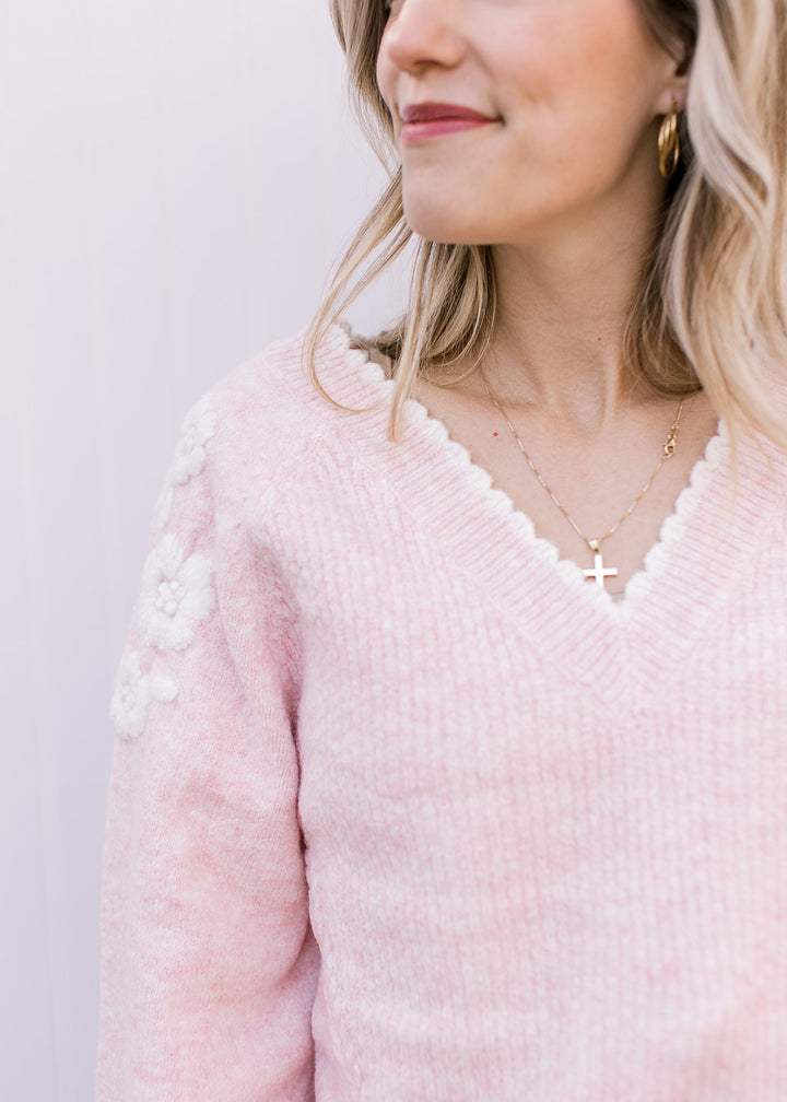 Close up of v-neck with white scalloped trim on a soft pink sweater with ribbing and long sleeves. 