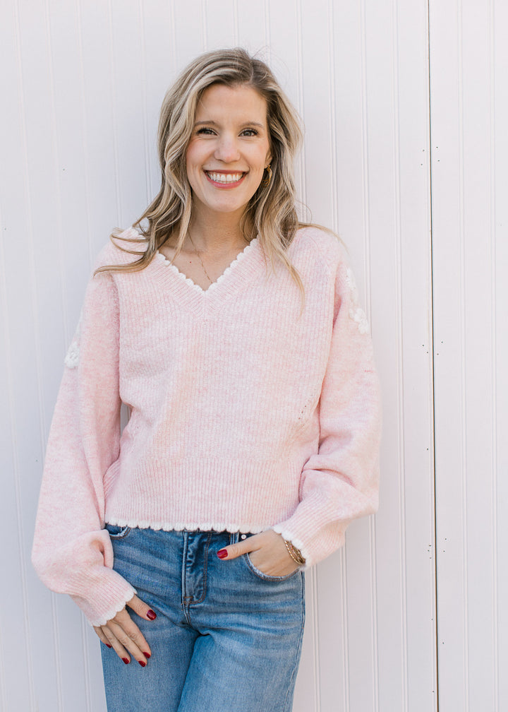 Model wearing jeans and a soft pink long sleeve sweater and a yarn floral embroidery at shoulder