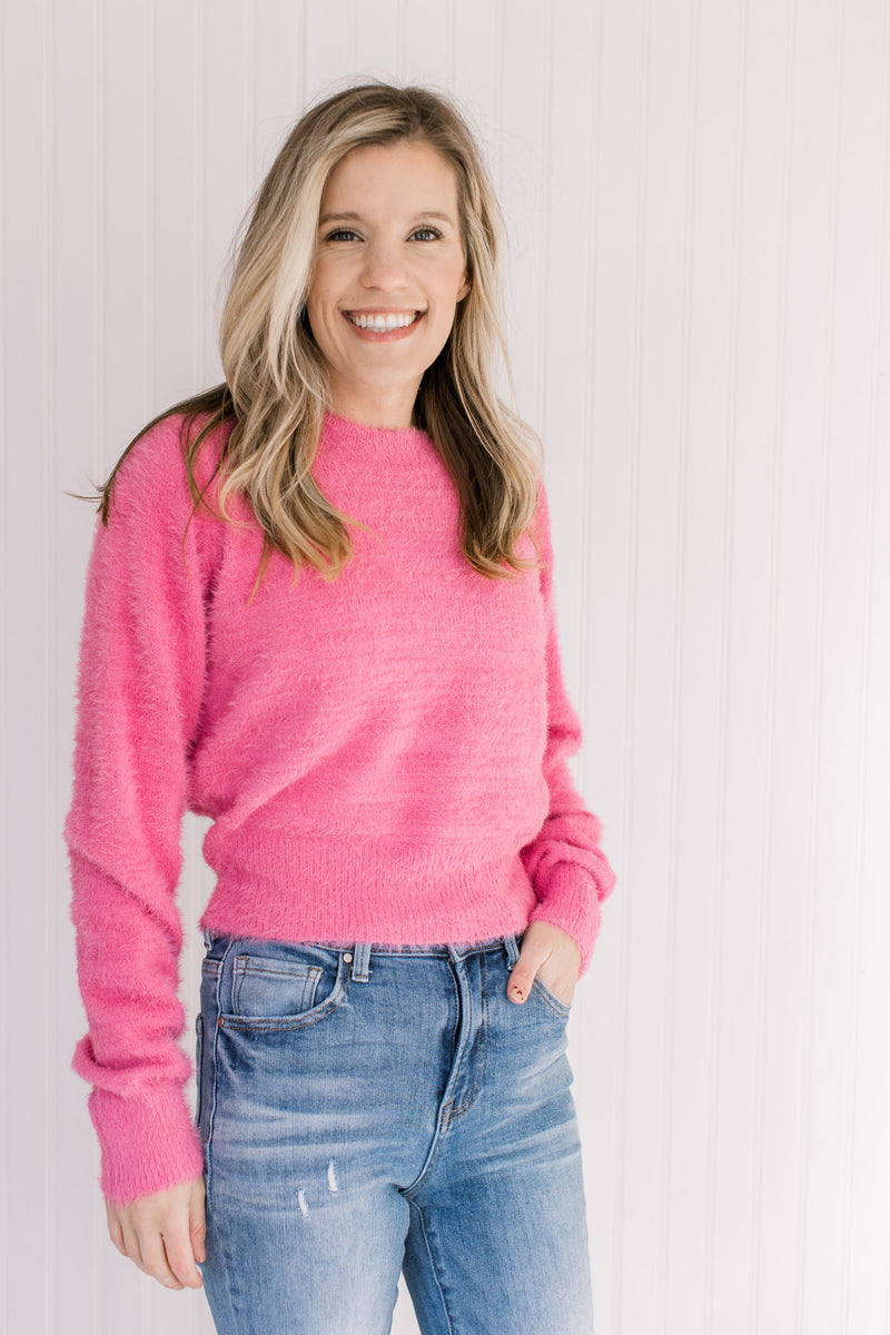 Model wearing a pink fuzzy sweater with a slightly cropped fit, long sleeves and a round neck.