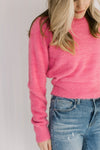 Close up of fuzzy material on a pink slightly cropped sweater with long sleeves and a round neck. 