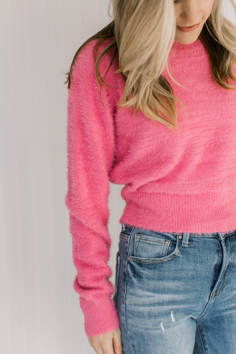 Close up of fuzzy material on a pink slightly cropped sweater with long sleeves and a round neck. 
