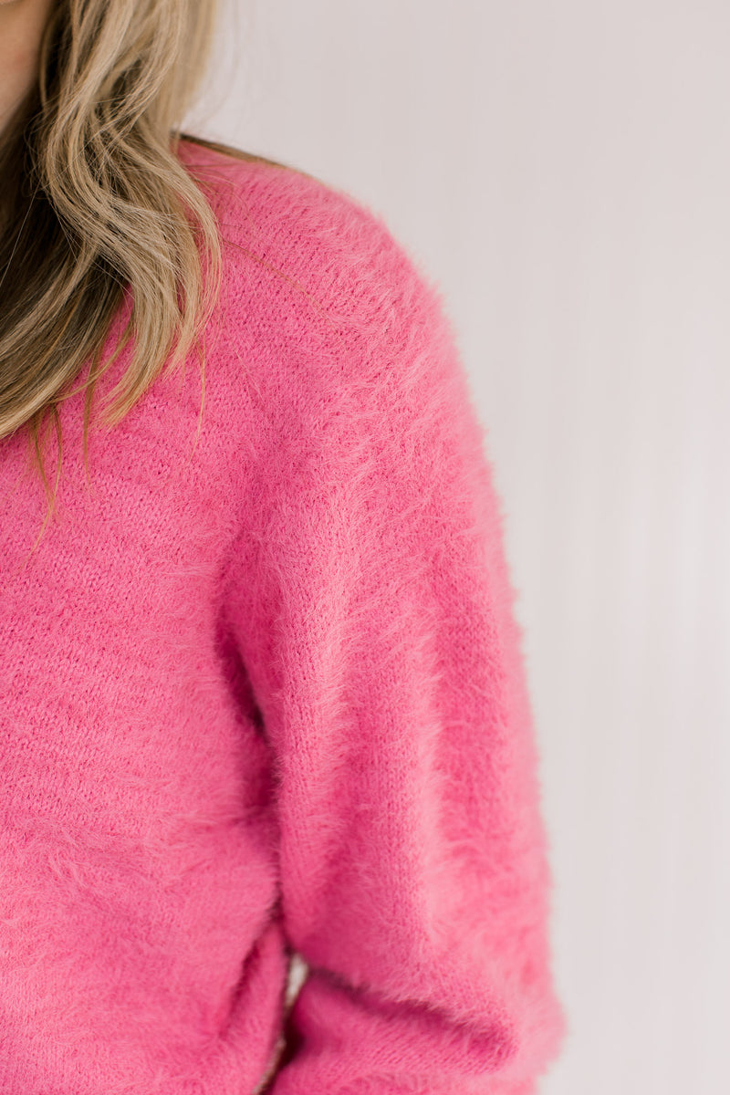 Close up of fuzzy material on a pink slightly cropped sweater with long sleeves and a round neck.