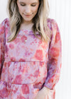 Model wearing a pink top with a blurred floral pattern, square neckline and sheer 3/4 sleeves. 