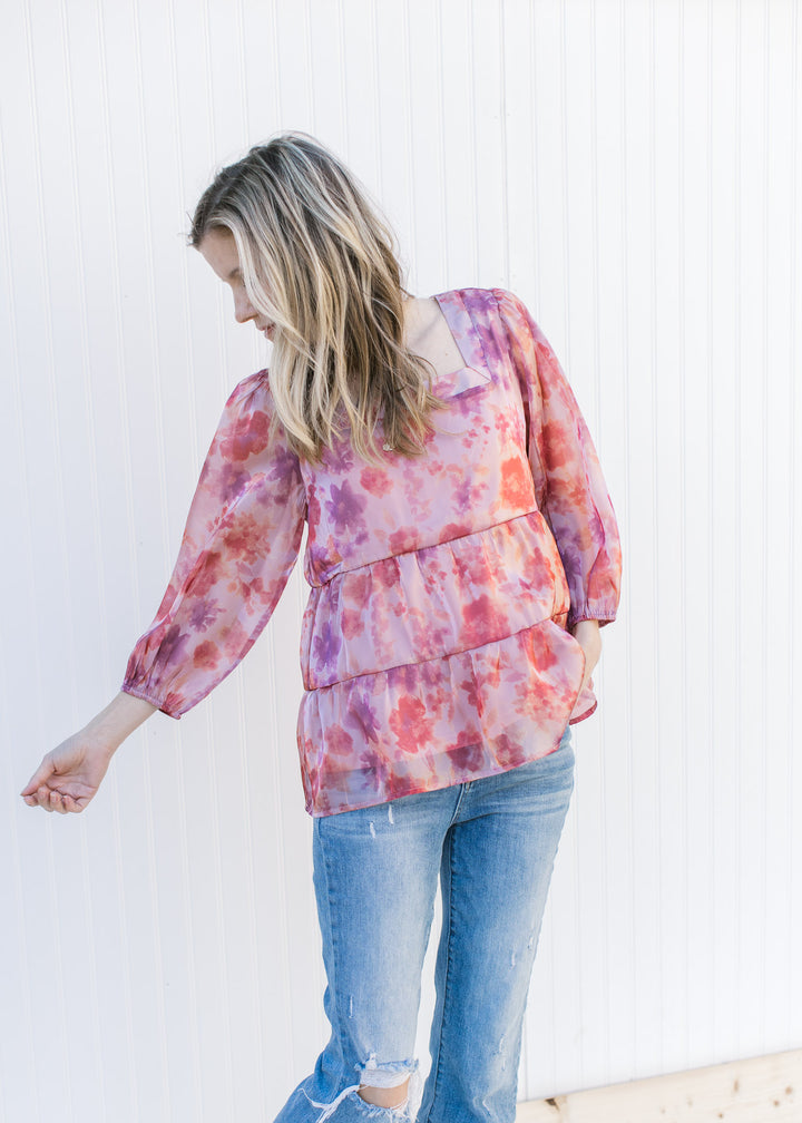 Model wearing a pink top with a shimmer material, blurred floral pattern and a square neckline.