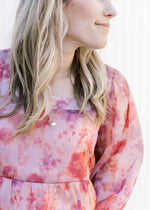Close up of square neck on a pink top with a slight shimmer and blurred floral pattern. 