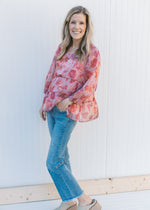Model wearing jeans, mules and a pink top with a blurred floral pattern and a square neckline. 