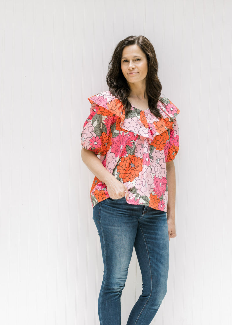 Model wearing jeans with a pink floral top with bubble short sleeves and a boat neck with a ruffle. 