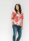 Model wearing a pink floral top with bubble short sleeves and a boat neck with a ruffle. 