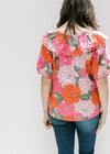 Back view of model wearing a fuchsia, red and pink floral top with bubble short sleeves. 