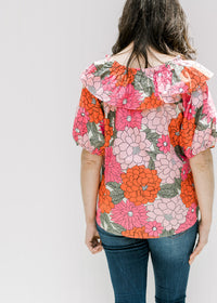 Back view of model wearing a fuchsia, red and pink floral top with bubble short sleeves. 